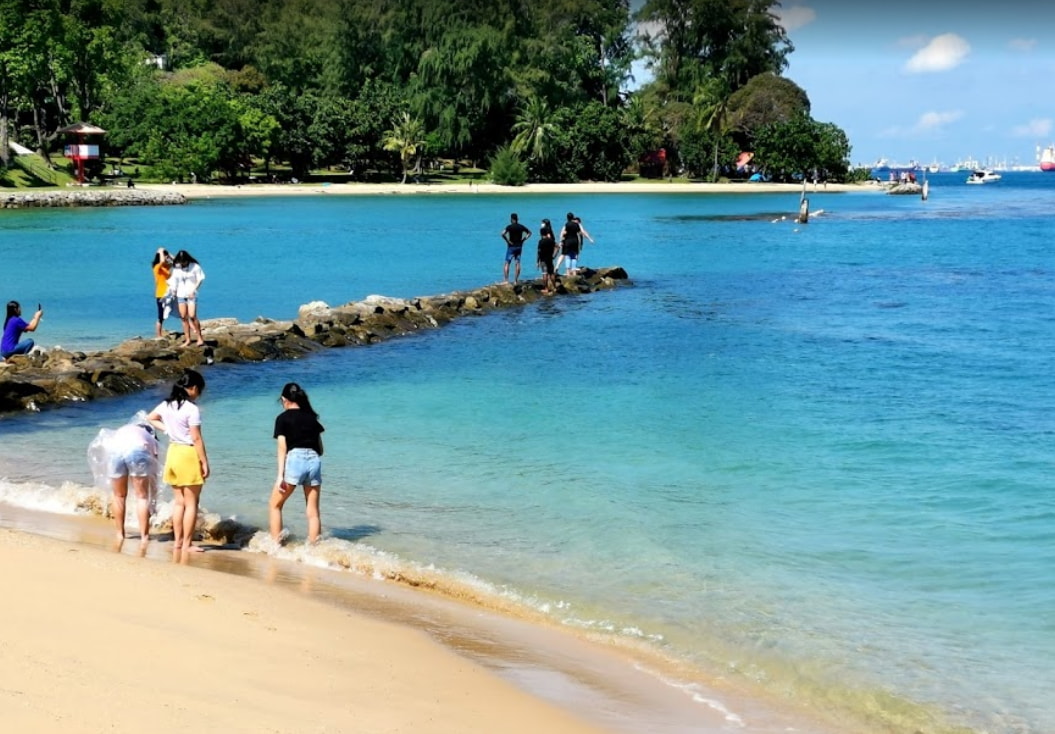 a rocky platform stretching out from st john's island beach in singapore, with people walking on it