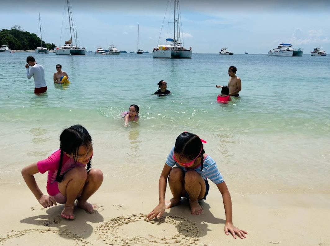 kids drawing in the sand on lazarus island's beach in singapore with yachts in the background